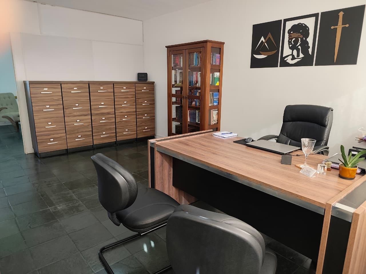 Sala de atendimento com arquivo de madeira, estante de livros e mesa de trabalho